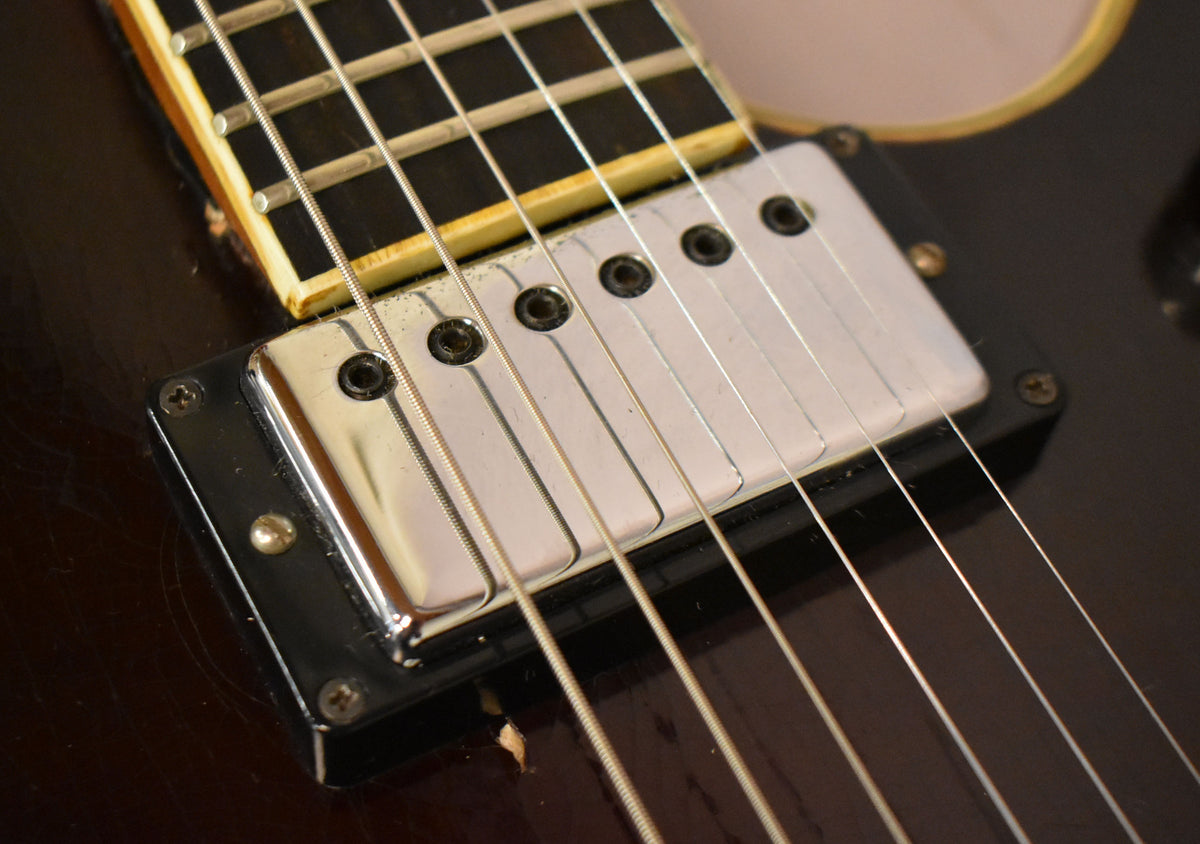 Close-up of the bridge pickup, showing its chrome cover, white inserts, and black surround, with visible finish wear and chips.