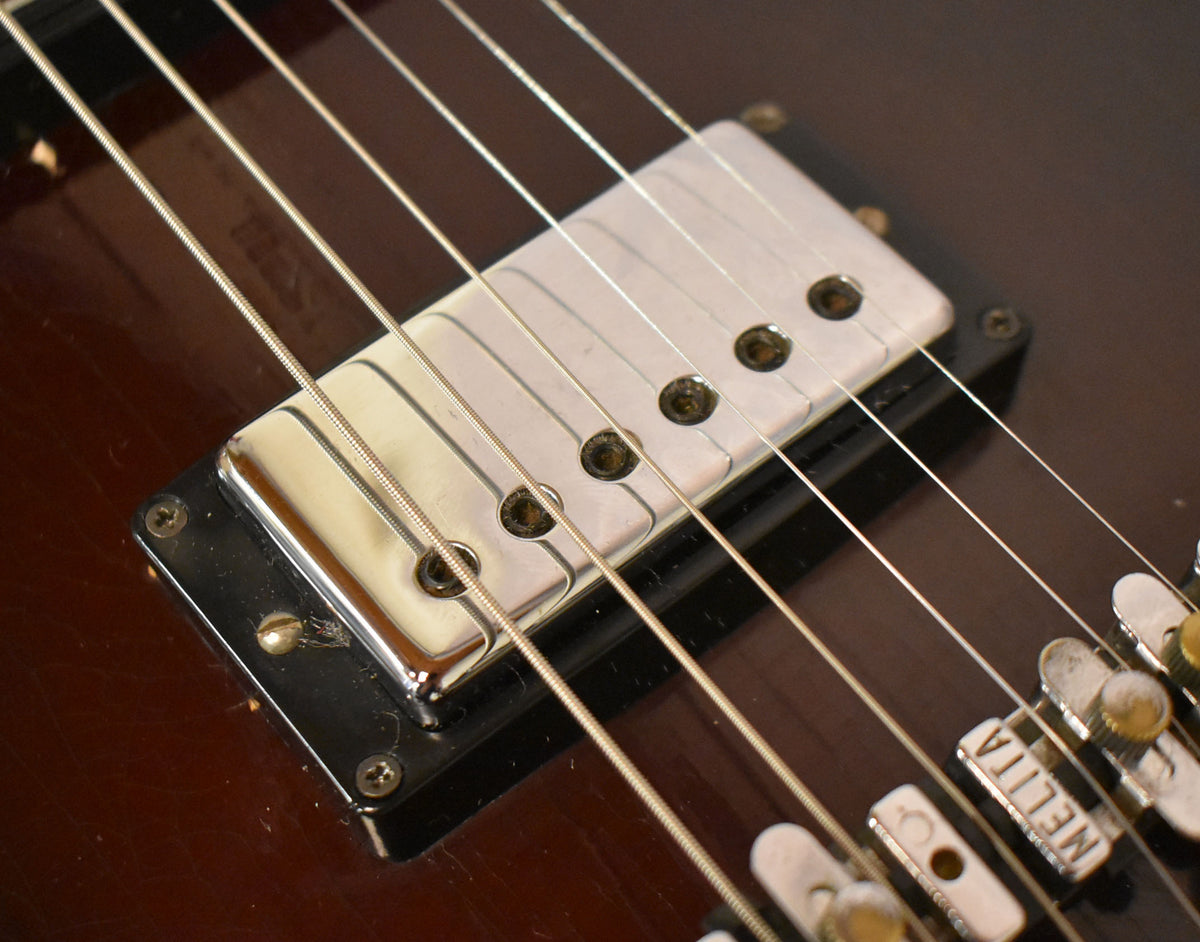 Close-up of the dark brown guitar body, showing a chrome pickup with six pole pieces and a Melita bridge.