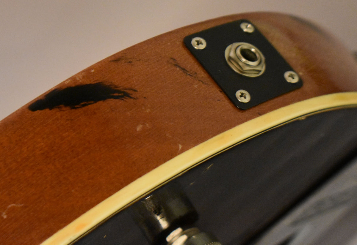 Close-up of the guitar's lower bout, showing the output jack on a black plate, with a large black paint chip on the brown side.