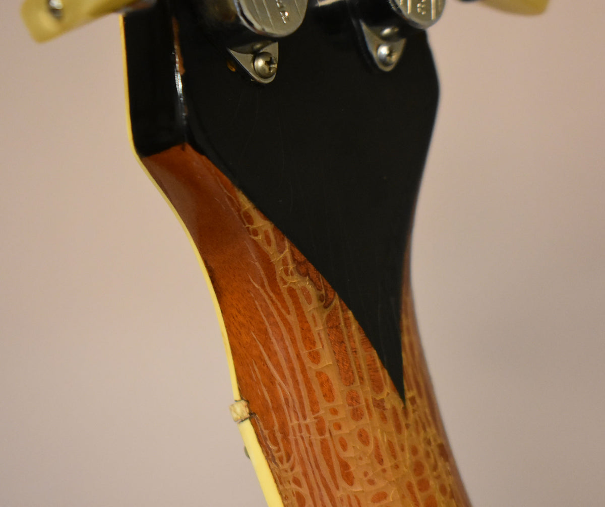 Close-up of the guitar's neck heel, showing heavy finish checking and wear on the brown wood, meeting a black headstock.