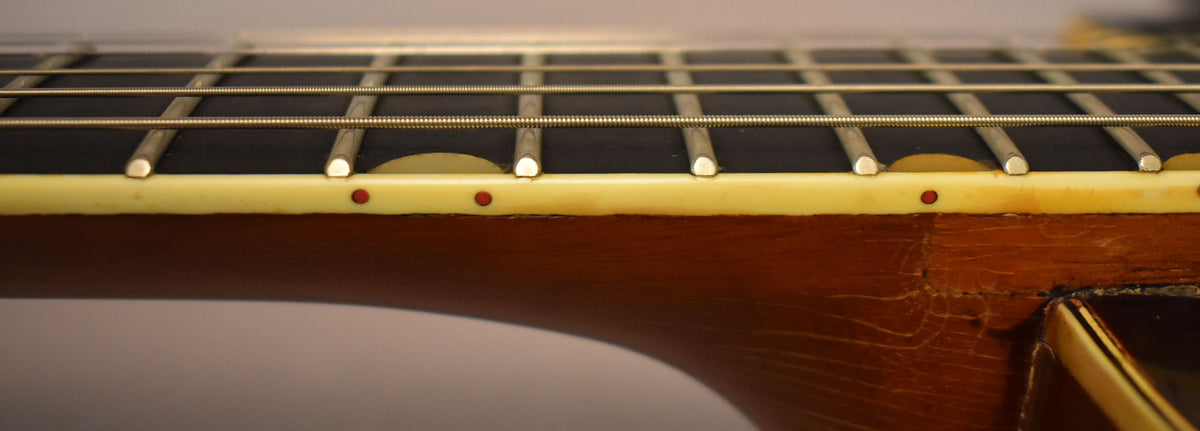 Close-up of the guitar neck, showing the dark fretboard, cream binding with red side dots, and a worn, dark brown neck heel.