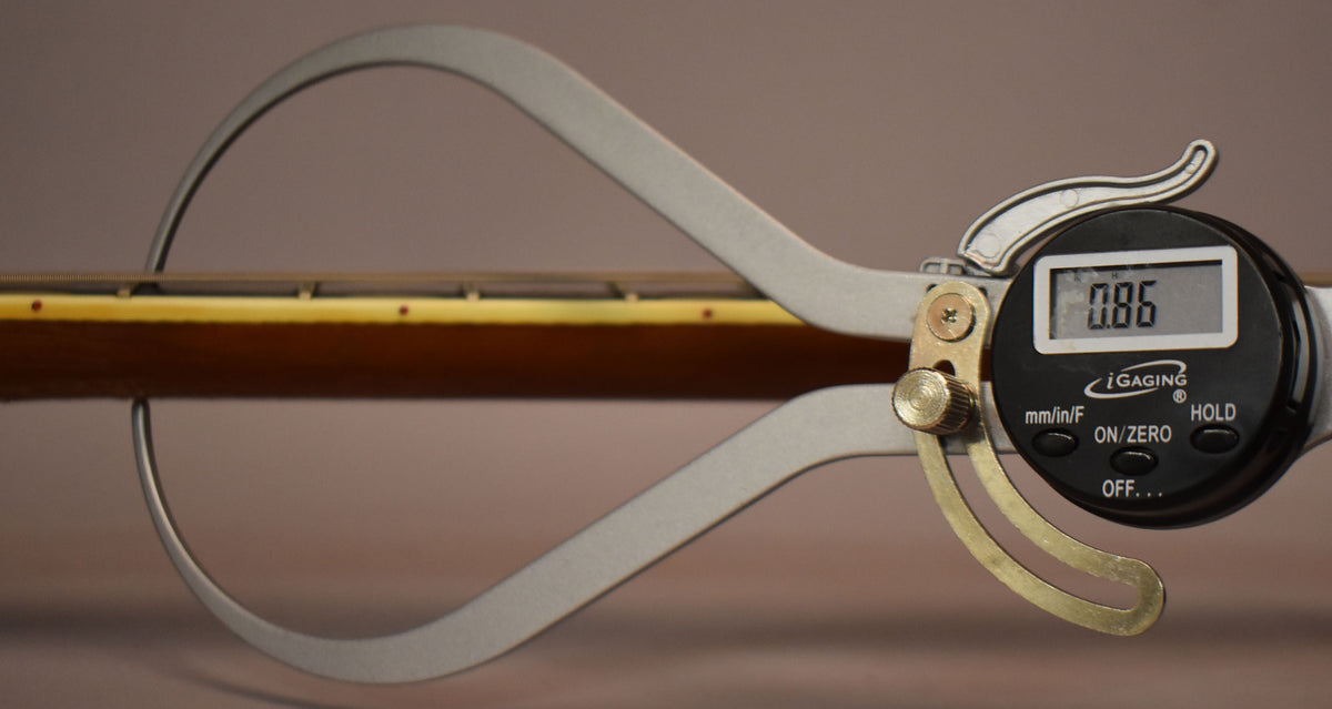 A digital caliper measures the guitar neck, showing a reading of 0.86, with the fretboard and side dots visible.