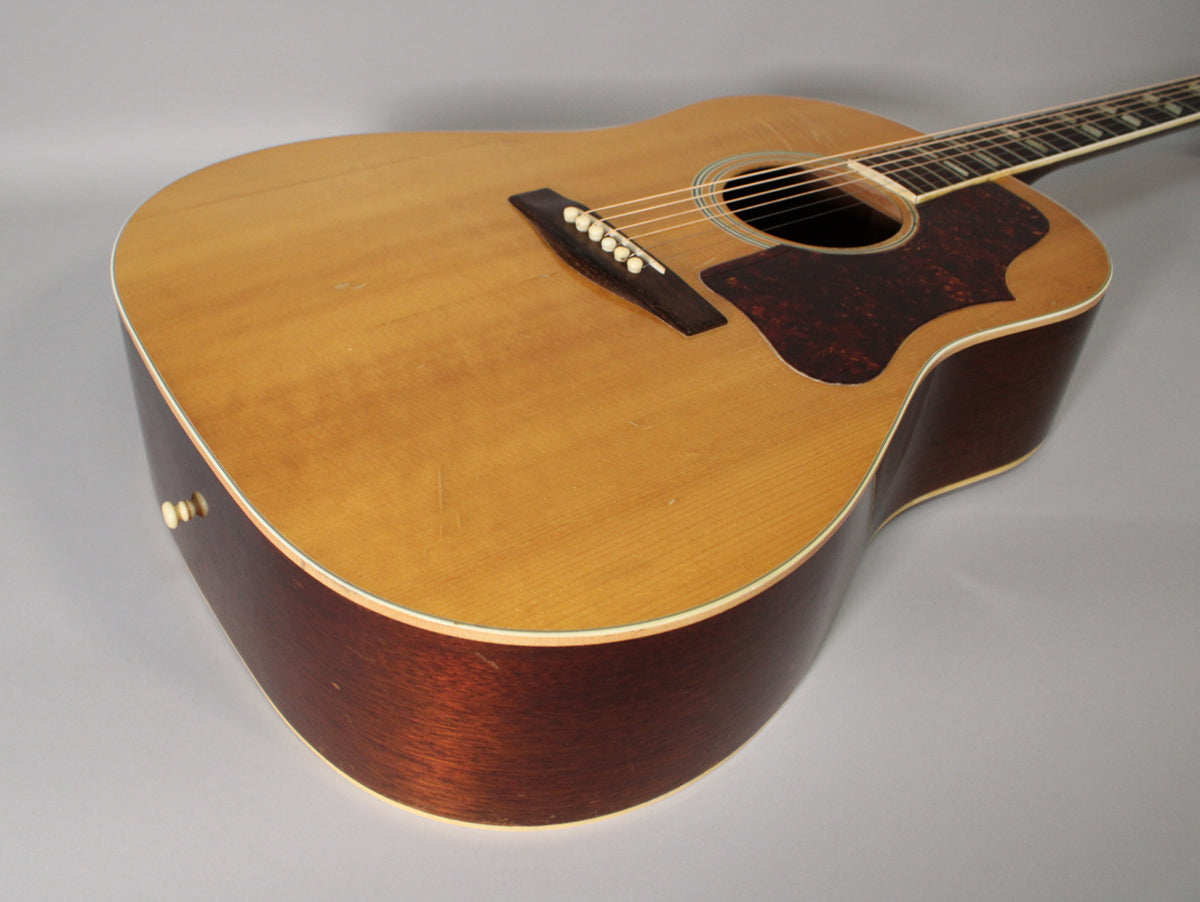 The acoustic guitar's natural finish top shows light wear and checking, with dark reddish-brown sides and a tortoiseshell pickguard.