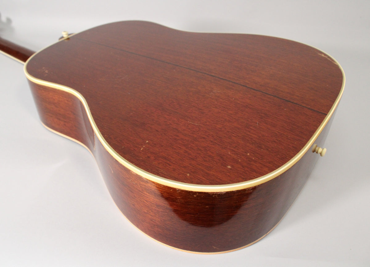 The back and side of a dark reddish-brown acoustic guitar are shown, with cream binding and visible finish wear and checking.