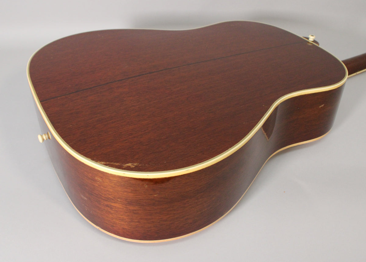 The back of the dark brown acoustic guitar, showing a center seam, light binding, and some finish wear on the lower bout.