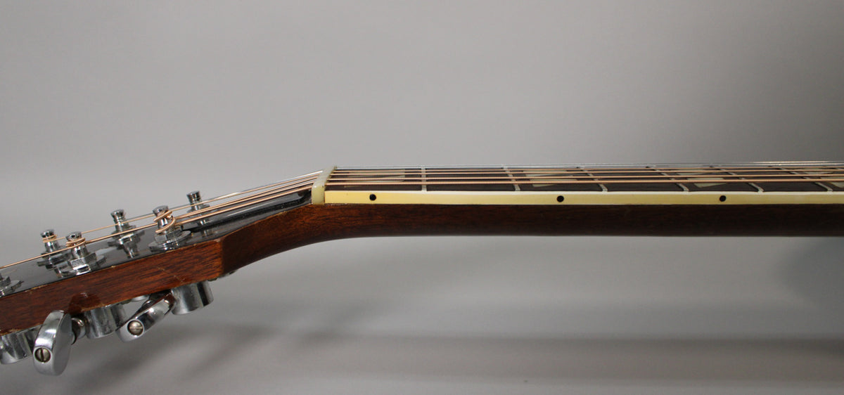 The guitar's dark brown neck and headstock are viewed from the side, showing six chrome tuners and cream binding along the fretboard.