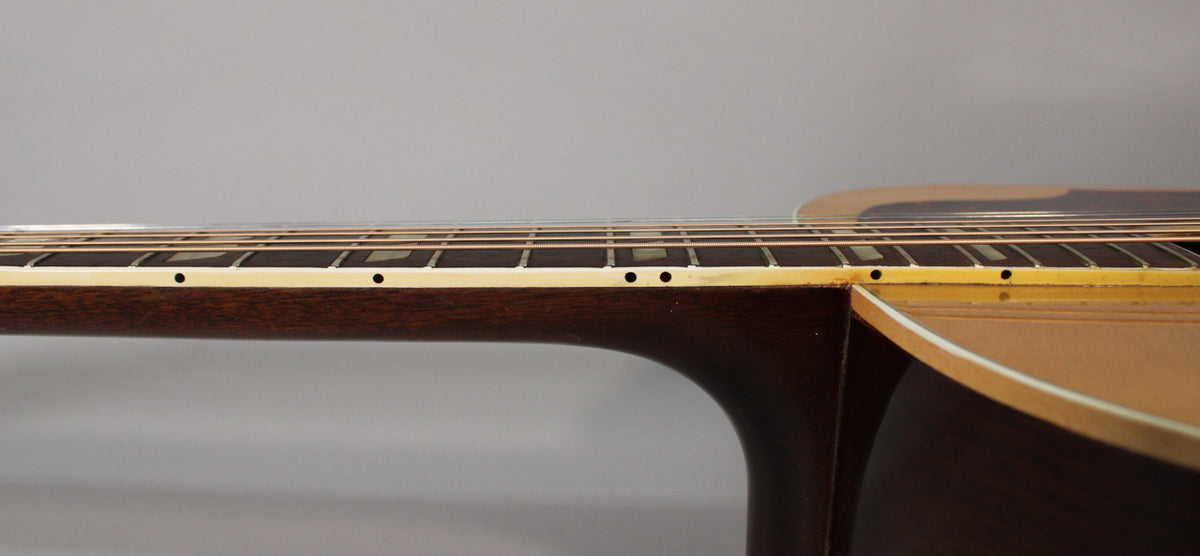 A side view of the guitar neck, showing the dark fretboard with rectangular inlays and cream binding, joining the natural body.