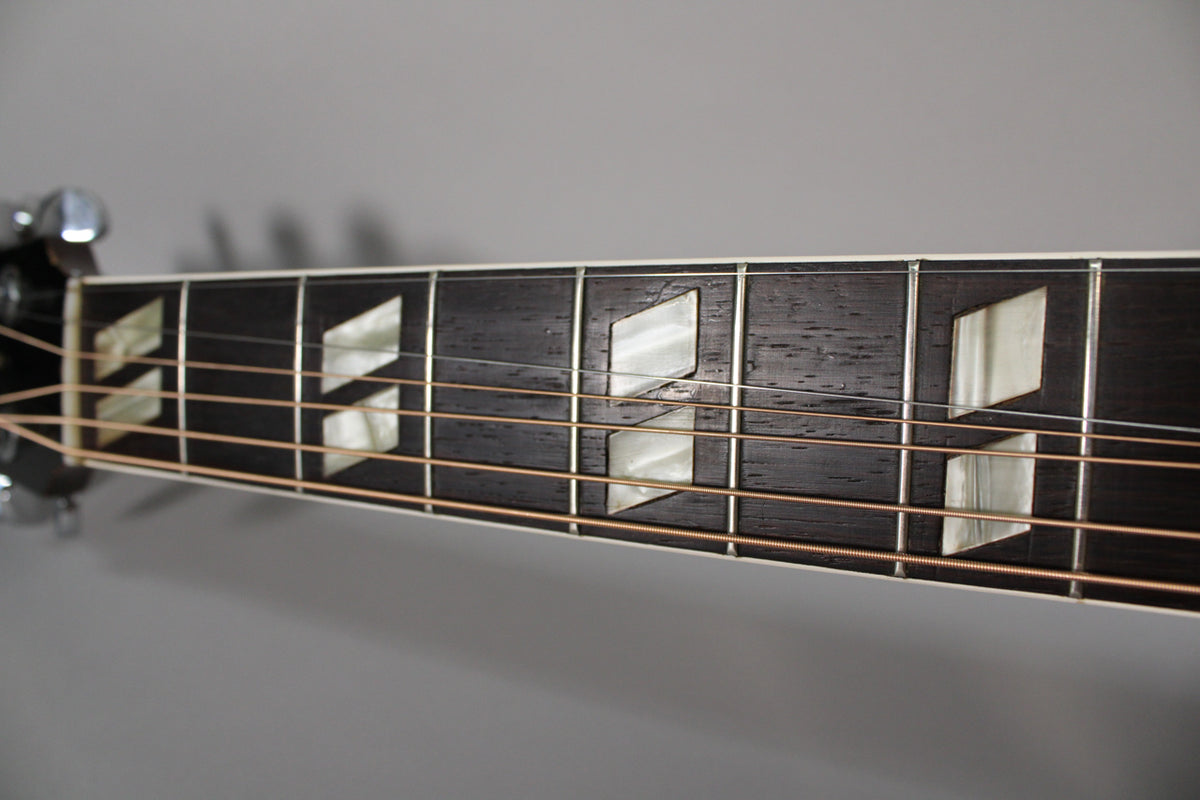 Close-up of the dark fretboard with mother-of-pearl parallelogram inlays, showing light wear and copper strings.