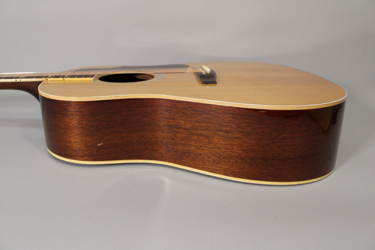 The acoustic guitar's natural spruce top and dark mahogany sides are visible from the upper bout, with a small ding on the lower bout.