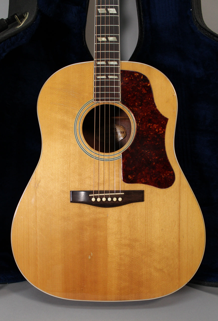 Full front view of a natural finish acoustic guitar with a tortoiseshell pickguard, showing some light wear on the body.