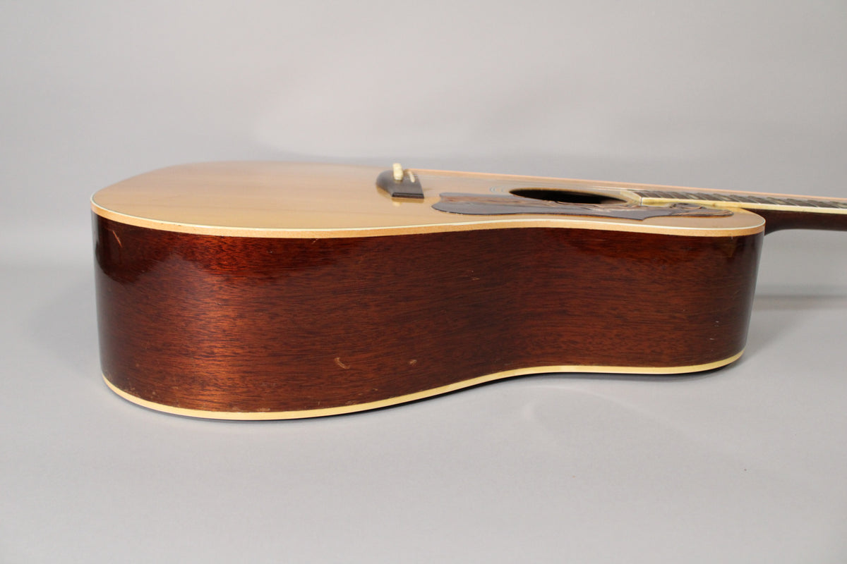The acoustic guitar's light-colored top and dark reddish-brown sides show visible wear and binding along the edges.