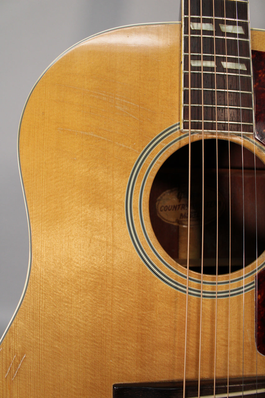 Close-up of the natural finish acoustic guitar's upper bout, showing pick scratches, the soundhole, and part of the fretboard.