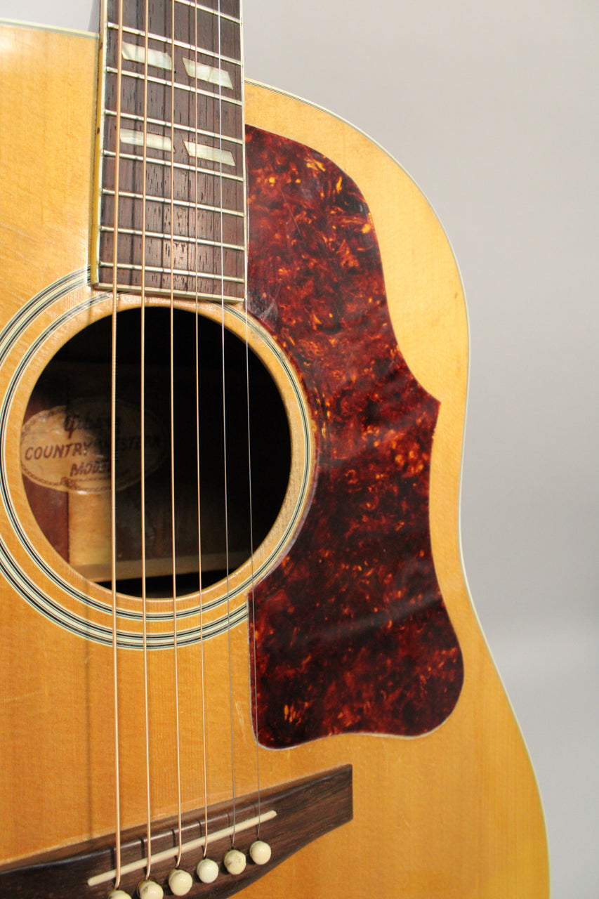 Close-up of the natural finish acoustic guitar's body, showing the tortoise pickguard, soundhole, and lower fretboard with block inlays.