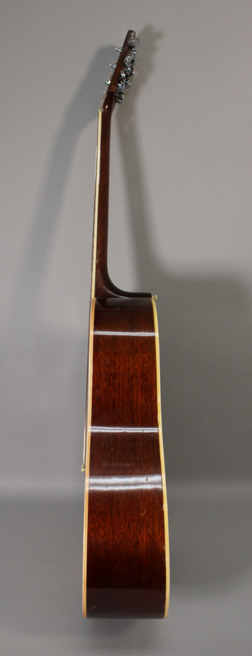 The acoustic guitar is shown from the side, revealing the dark brown body and neck, with light binding and chrome tuners.