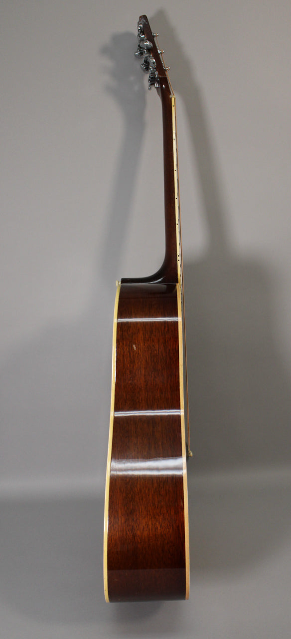 The acoustic guitar is shown from the side, revealing the dark brown body with cream binding and a few minor scuffs.