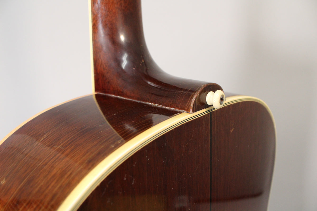 Close-up of the guitar's dark brown neck heel and body, showing a cream end pin, binding, and finish checking.