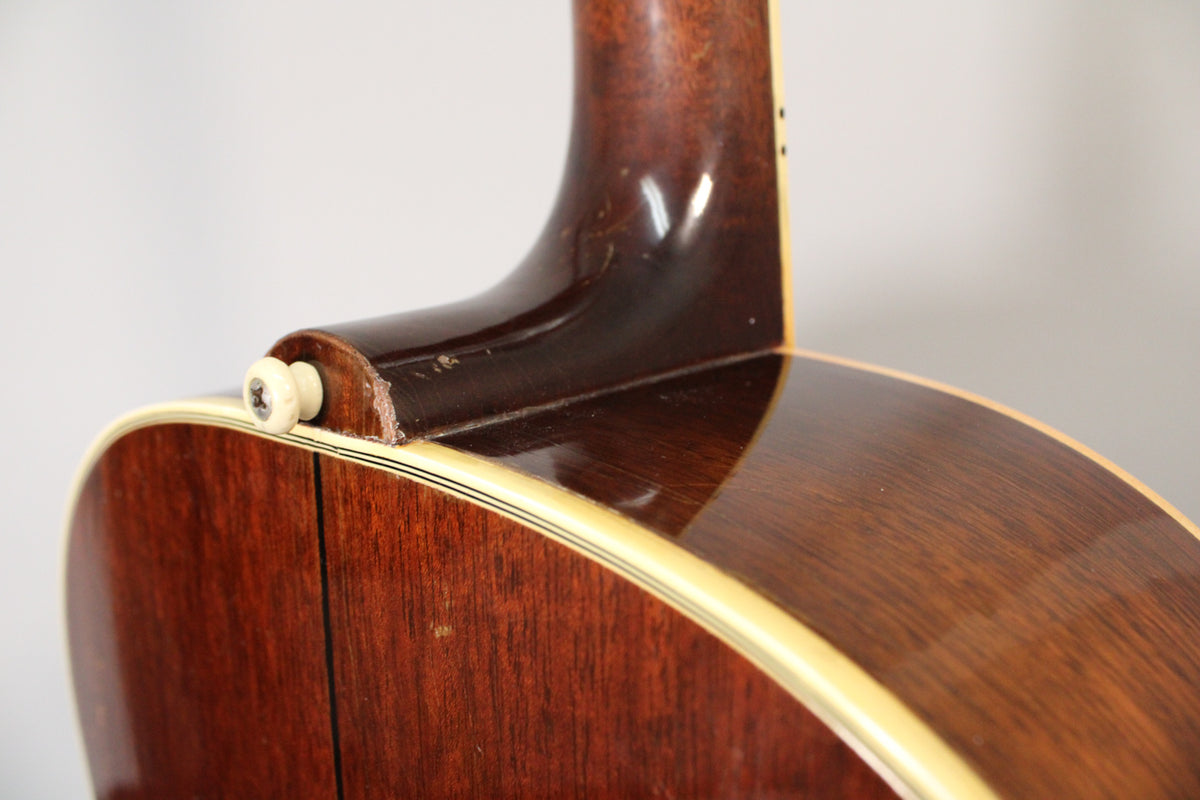 Close-up of the guitar's dark brown neck heel and body, showing a cream end pin, binding, and finish wear.