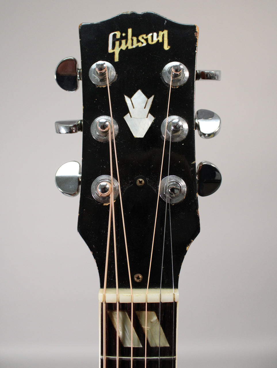 Close-up of the black headstock with gold lettering, six chrome tuners, mother-of-pearl crown inlay, and trapezoid fretboard inlays.