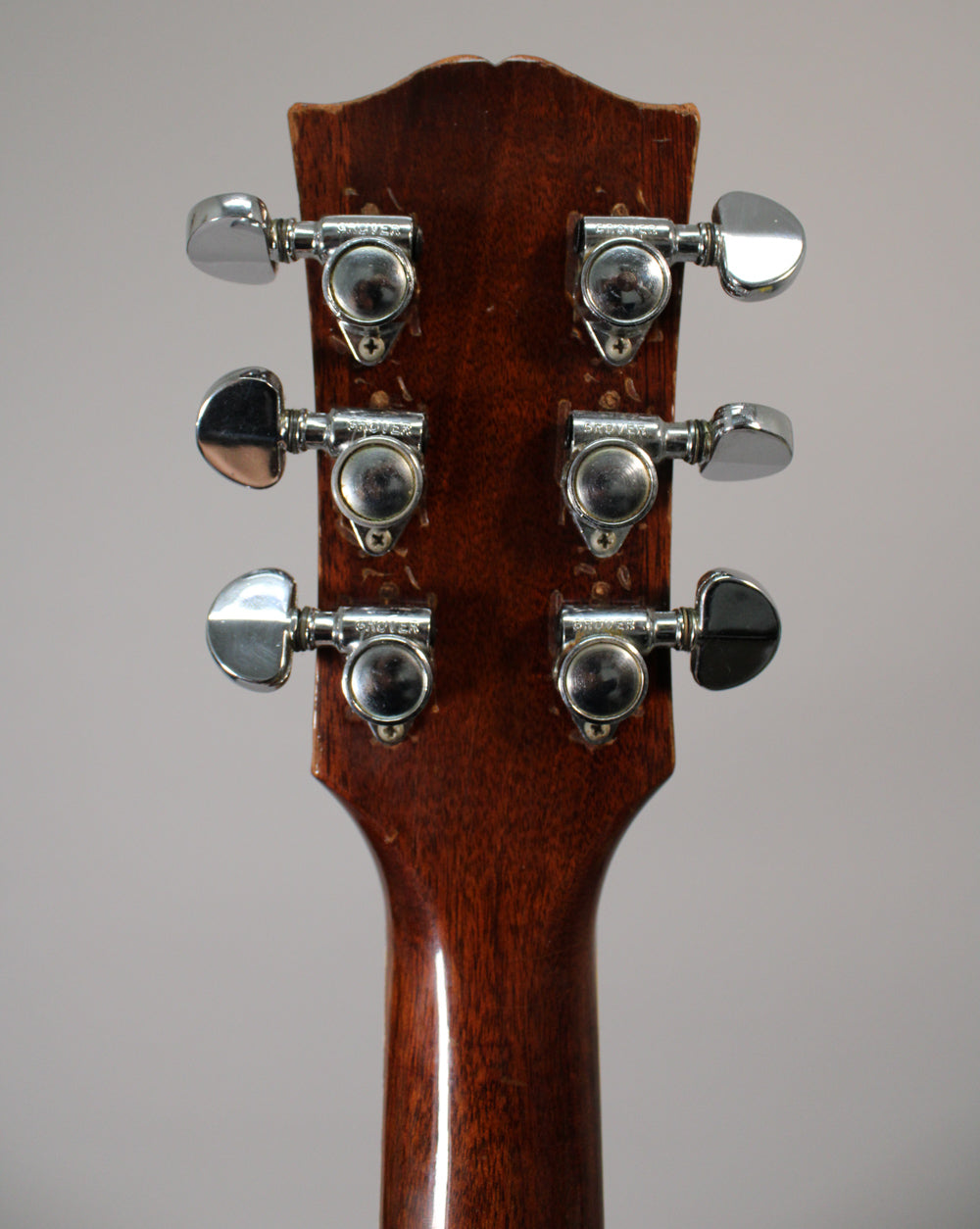 Rear view of the guitar's headstock and upper neck, showing six chrome tuners on a dark brown finish with visible wear.