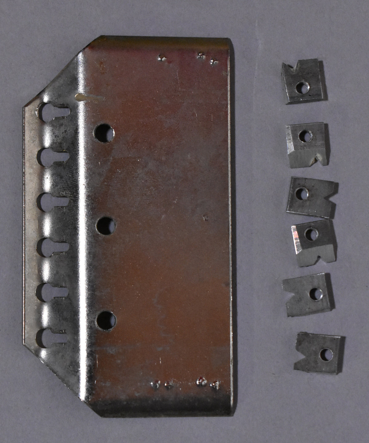 Full top-down view of the guitar's chrome tailpiece with six string slots and six small metal inserts, showing minor surface scratches.