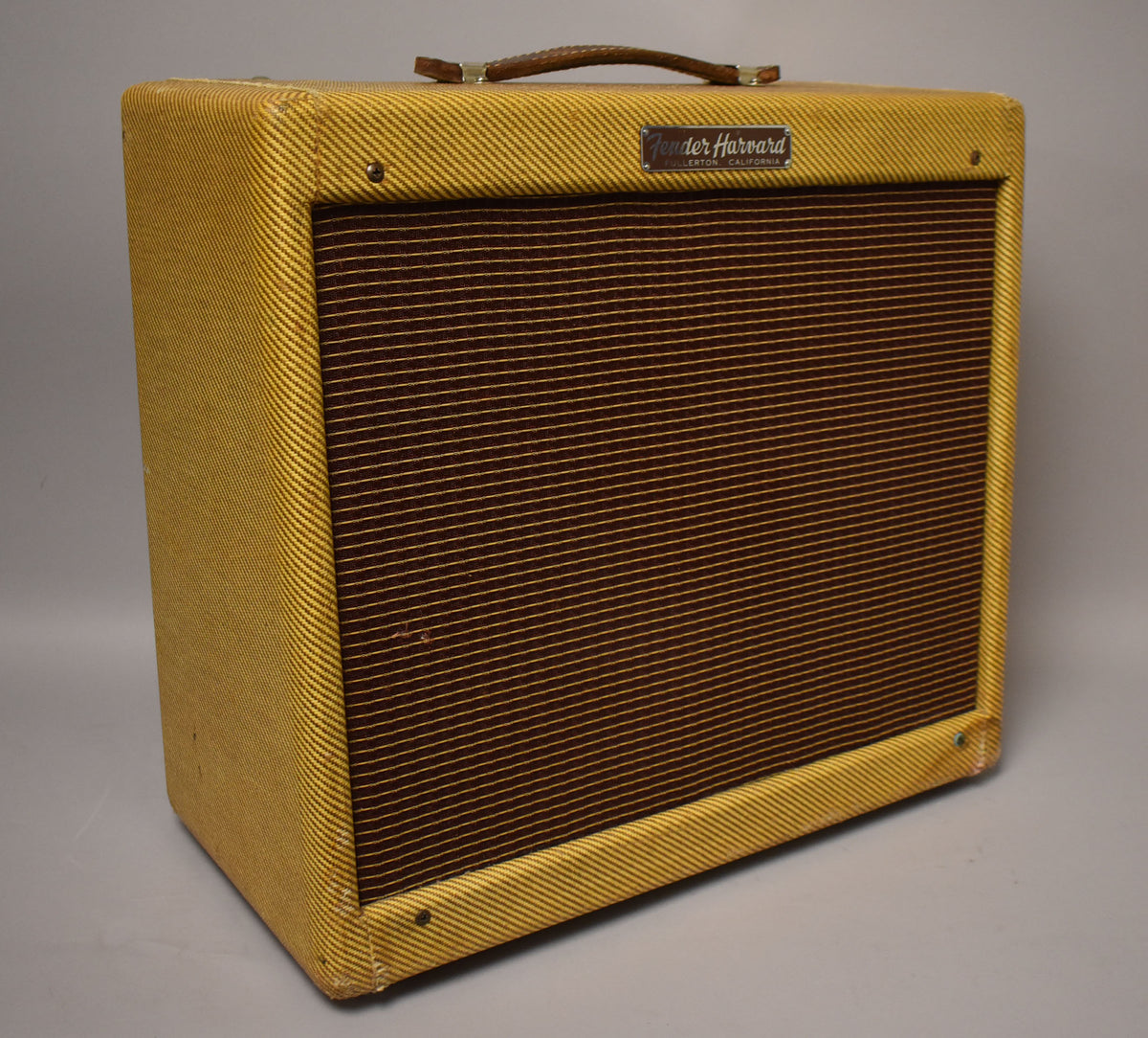 A tweed combo amp, angled to show the front and left side, with a dark brown grille and a braided leather handle.