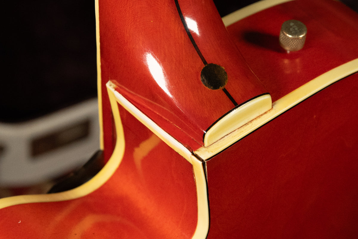 Close-up of the guitar's orange neck heel and body binding, showing a strap button and a small hole on the neck.