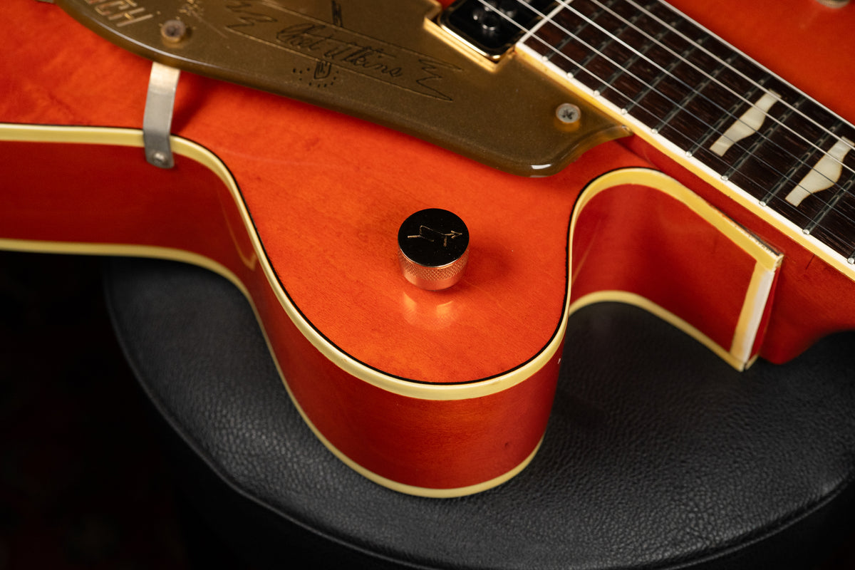 Close-up of the guitar's lower bout, showing the orange finish, cream binding, a single knurled control knob, and part of the pickguard.