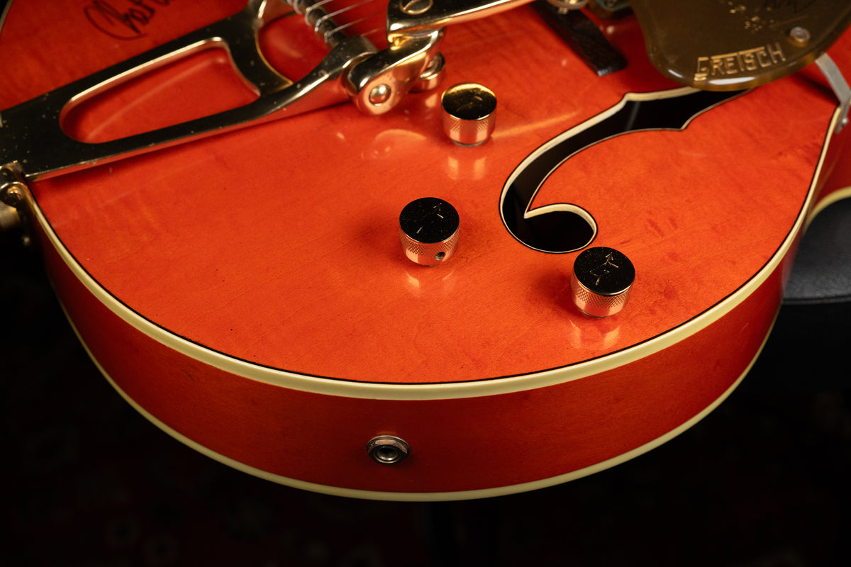 Close-up of the guitar's lower bout, showing the orange finish, gold hardware, three knurled control knobs, and an f-hole.
