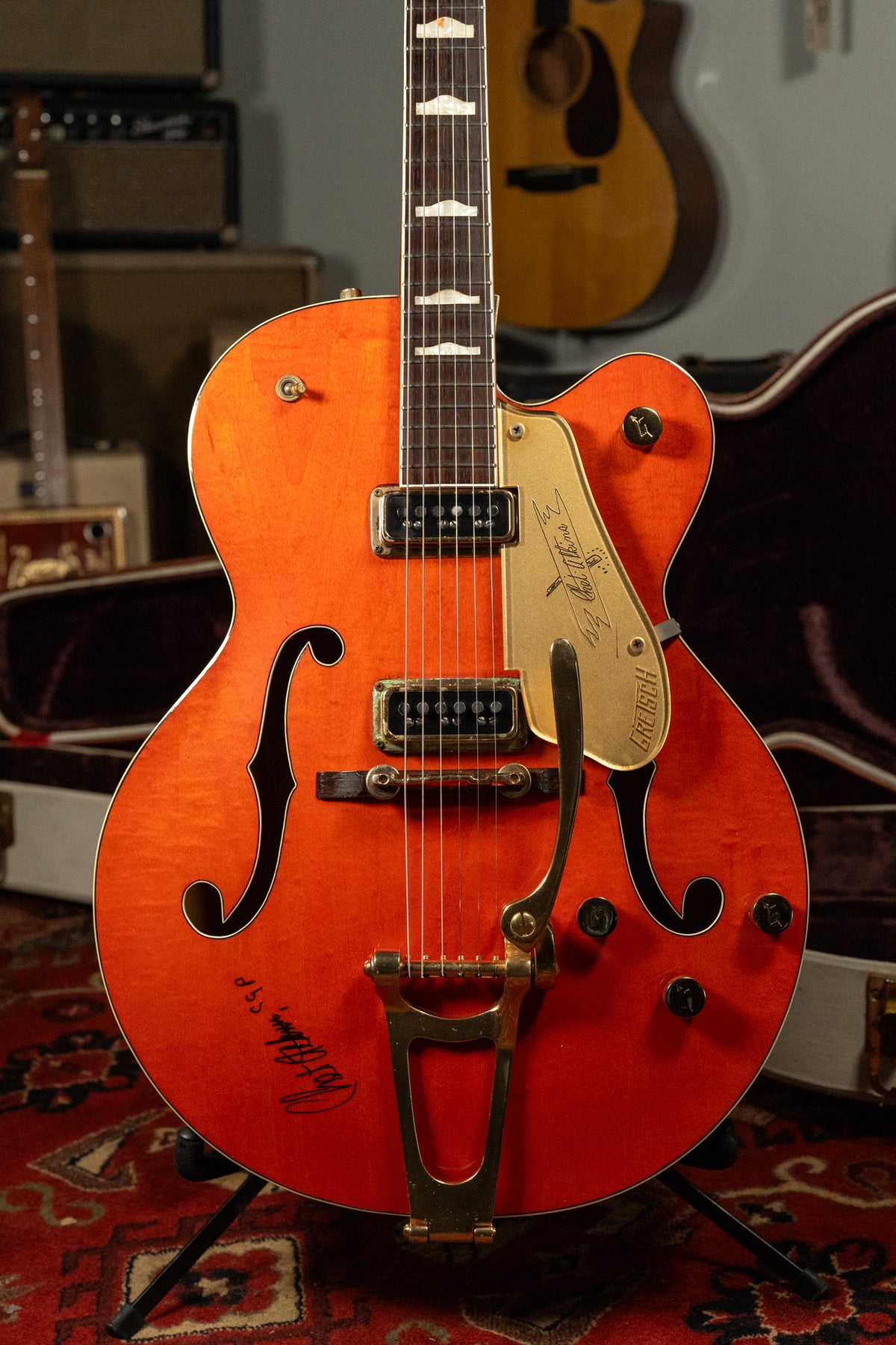 Full-frame, orange hollow-body electric guitar with f-holes, gold hardware, Bigsby tremolo, and a signature on the lower bout.