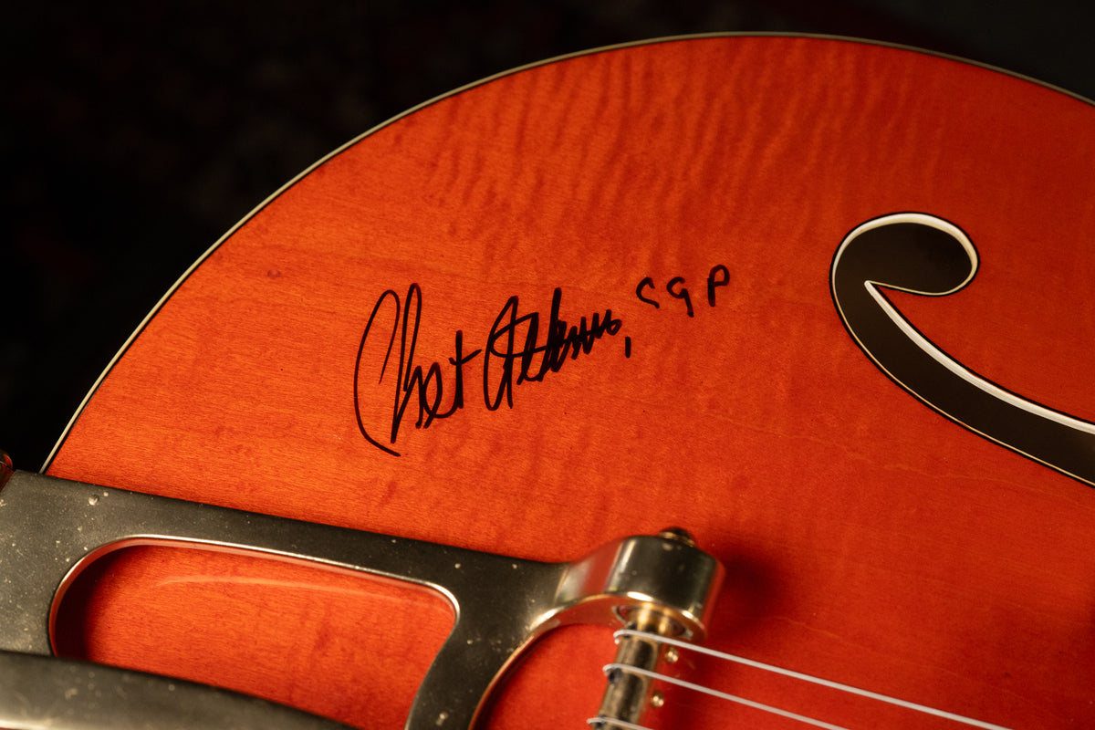 Close-up of the guitar's orange body, showing a black "Chet Atkins, CGP" signature, an f-hole, and part of a Bigsby tremolo.