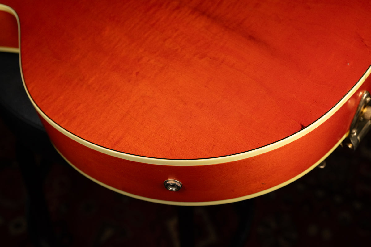 Close-up of the lower bout of the orange guitar body, showing the output jack, cream binding, and light finish checking.