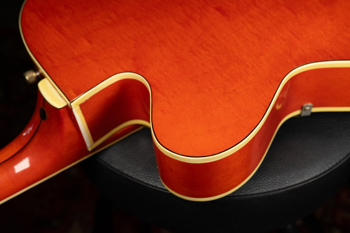 Close-up of the guitar's lower bout and cutaway, showing the orange finish with wood grain, cream binding, and light finish checking.