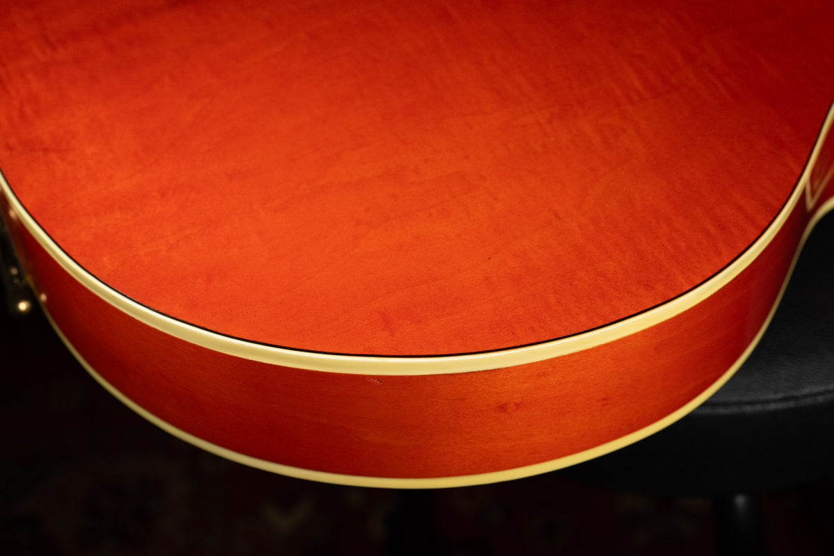 Close-up of the guitar's lower bout, showing the orange finish with wood grain, cream binding, and minor wear on the side.