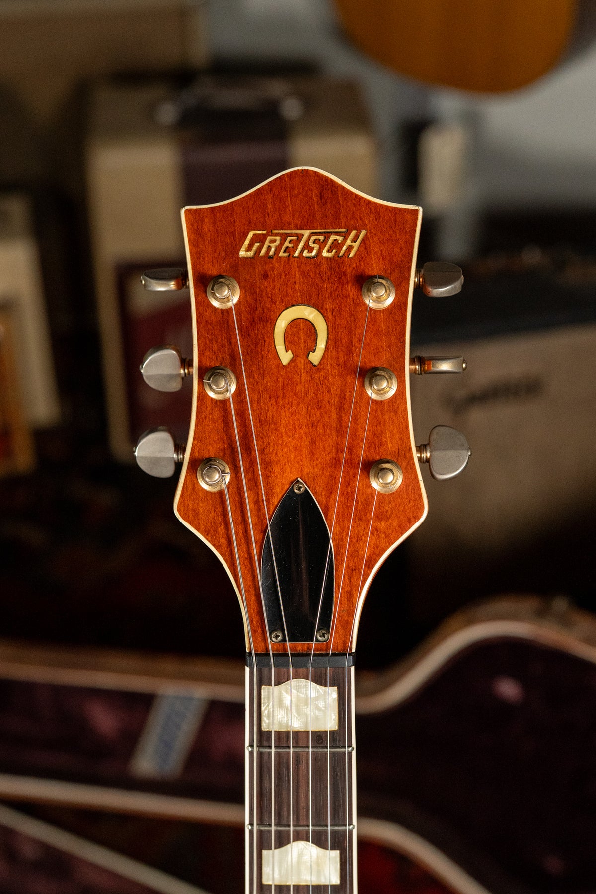 Close-up of the guitar's headstock, showing the orange-brown finish, gold logo, horseshoe inlay, six tuners, and part of the fretboard.