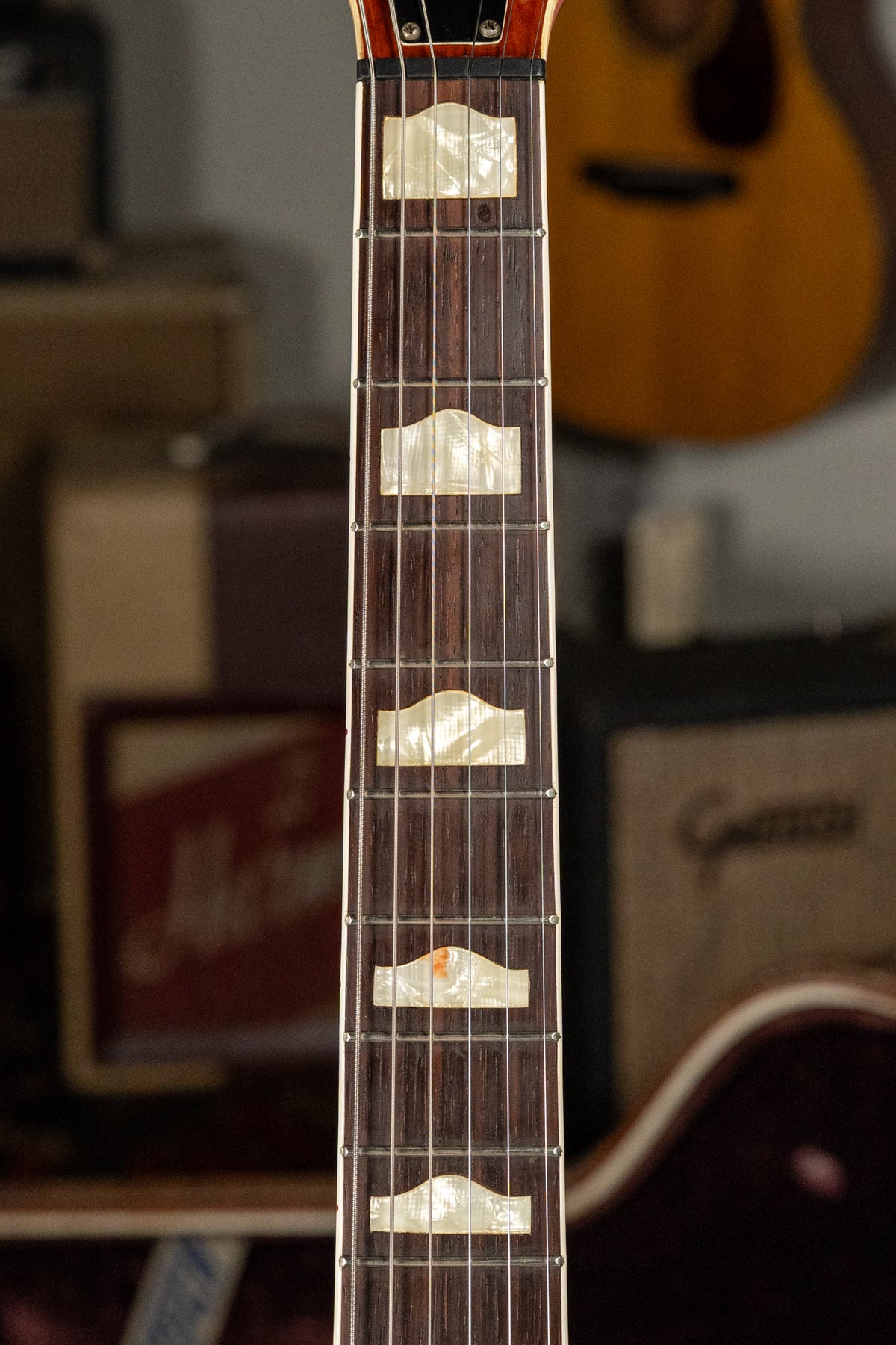 Close-up of the dark rosewood fretboard with mother-of-pearl hump block inlays, showing some wear and discoloration on the 7th fret inlay.