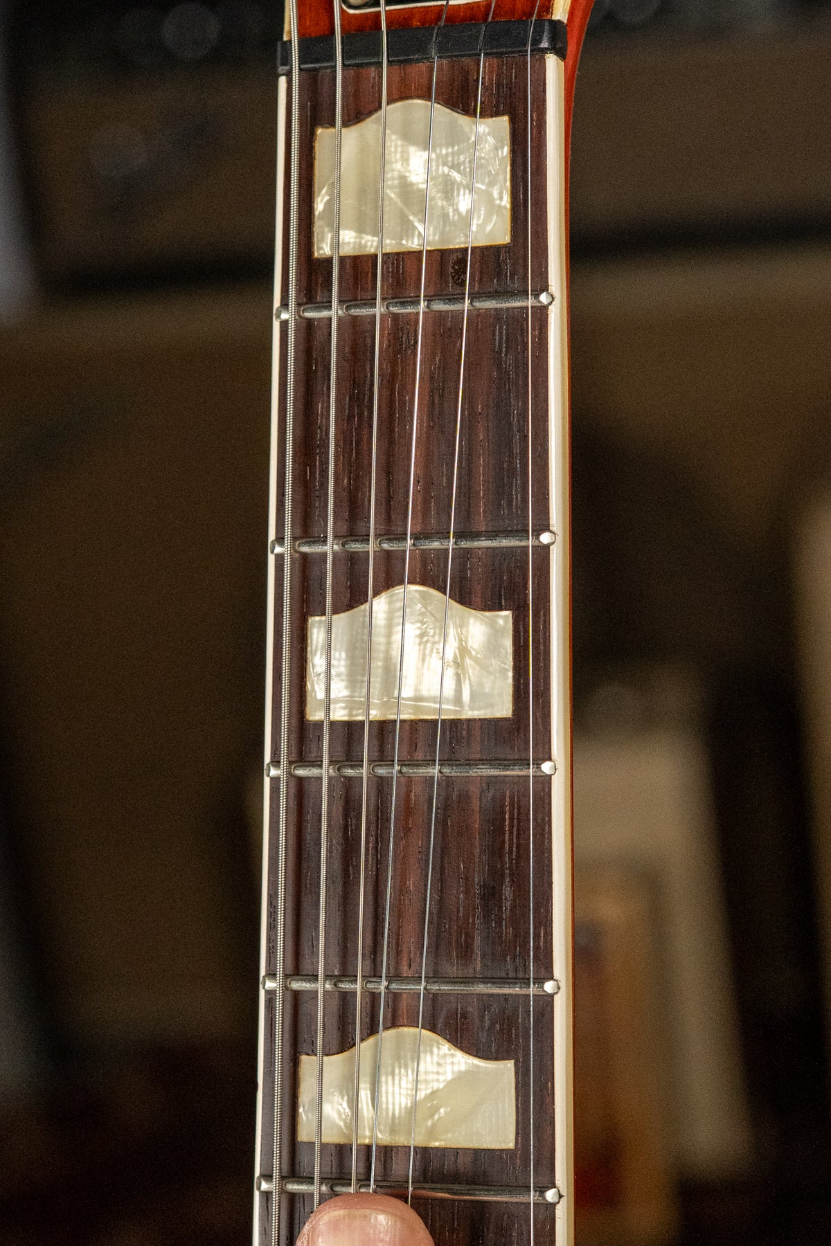 Close-up of the dark rosewood fretboard with three pearloid hump-block inlays and a hint of a finger on the lowest string.