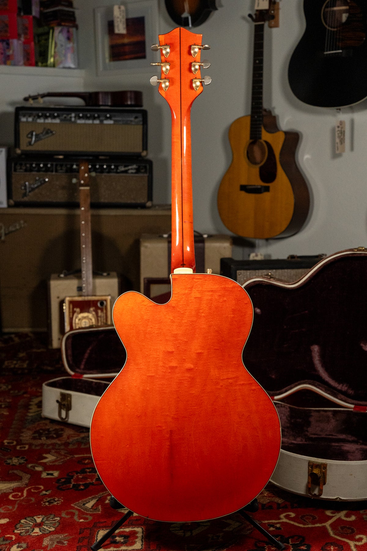 The back of an orange-finished hollow-body electric guitar with a flamed maple grain, showing light wear and six gold tuners.