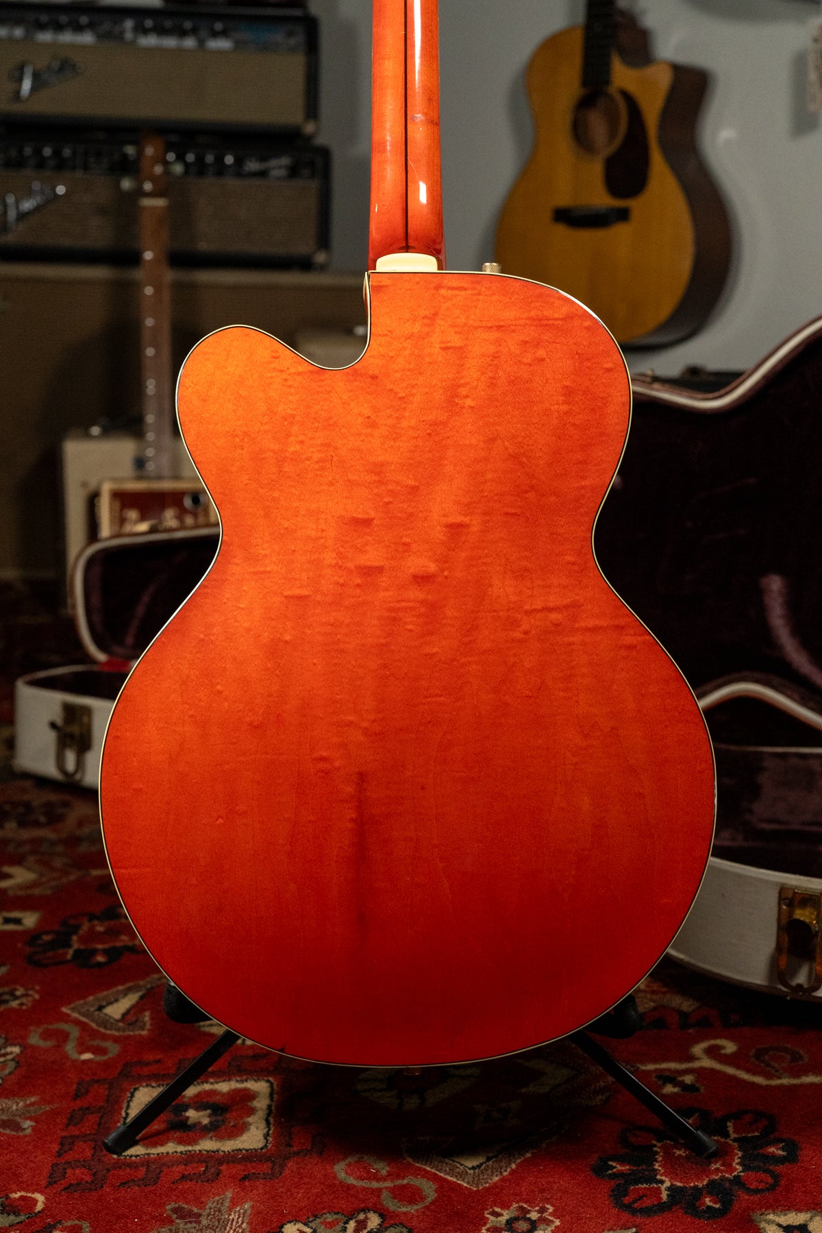 Full back view of the orange electric guitar, showing its flame maple body, white binding, and neck heel with a strap button.