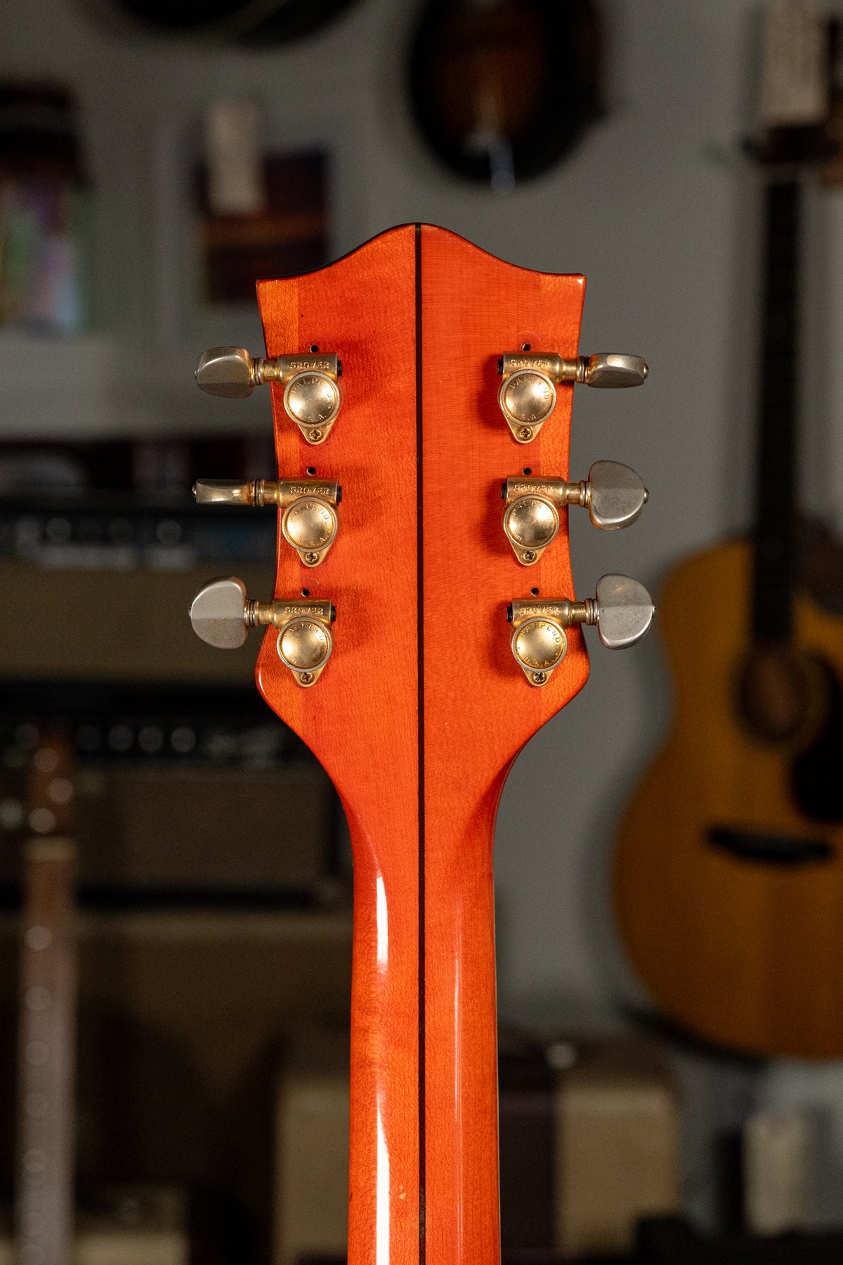 The back of the headstock and neck, showing a vibrant orange finish, six gold-plated tuners, and a visible center seam.
