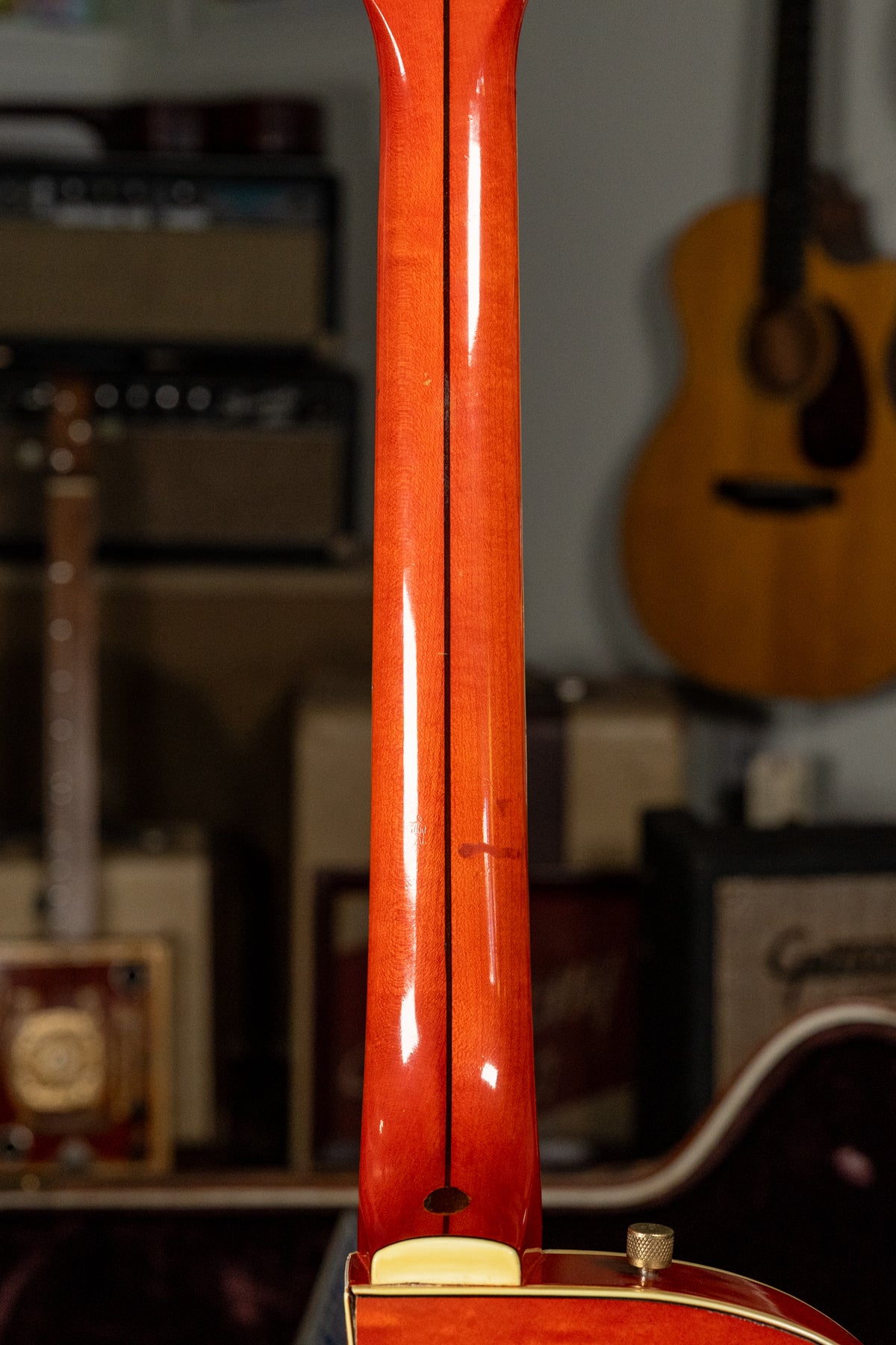 The guitar's glossy orange neck, with a dark center stripe, is viewed from behind, showing a small red mark and light wear.