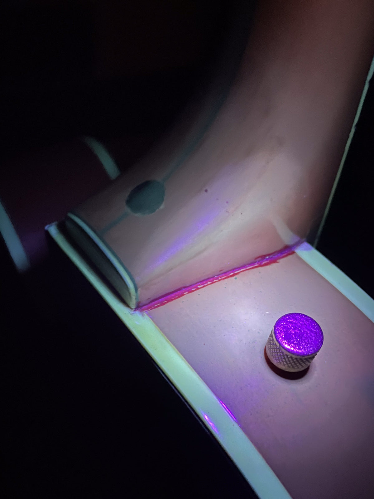 Close-up of the guitar's orange body under UV light, revealing a bright pink seam and a glowing purple knob.
