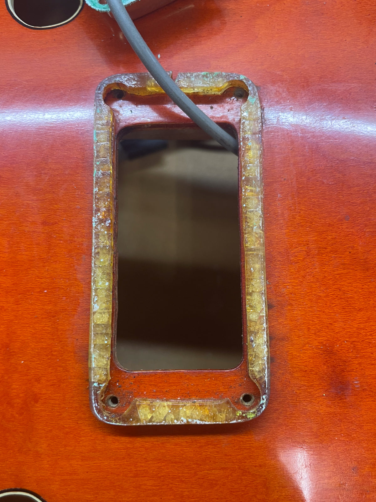 Close-up of the orange guitar body, showing a rectangular control cavity with a thick, aged, yellowed plastic trim and a grey wire.