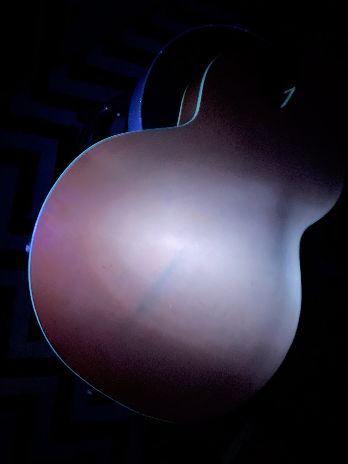 The guitar's orange finish body is seen from the back, with light reflecting off its center and subtle wear visible.