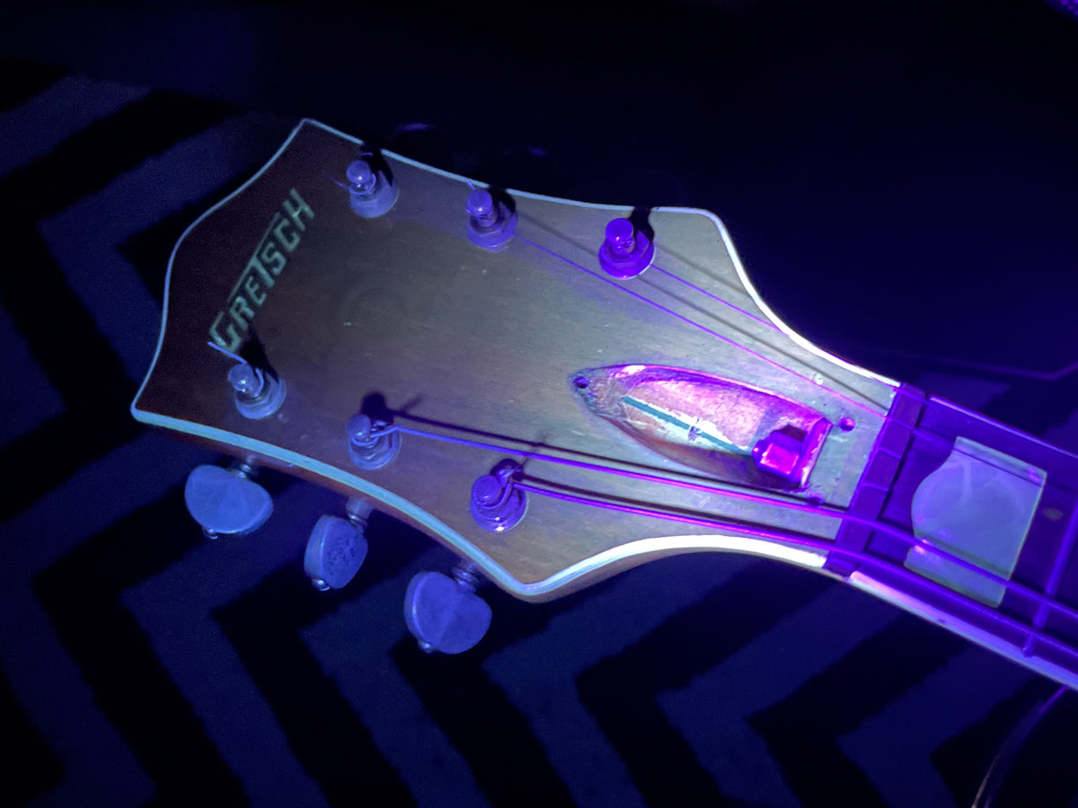 Close-up of the headstock, showing six tuners with cream buttons, a truss rod cover, and light wear on the natural finish.