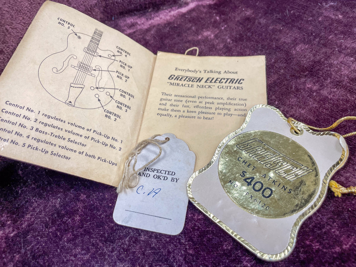 Open instruction manual with guitar diagram and a gold-trimmed hang tag showing "Gretsch Chet Atkins $400" on a purple surface.