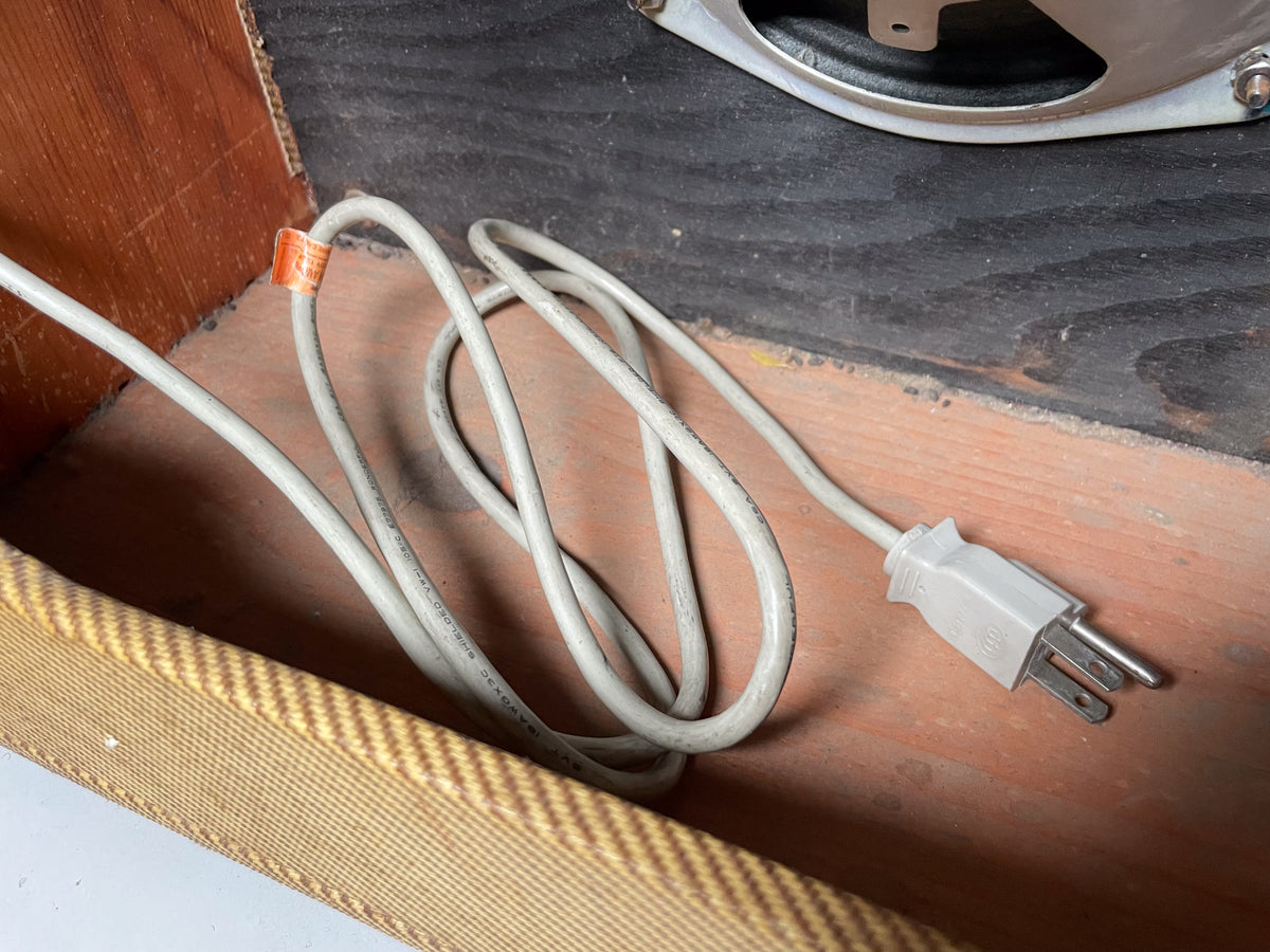 Close-up of the amp's interior, showing a coiled gray power cord with a three-prong plug, resting on the wooden base.