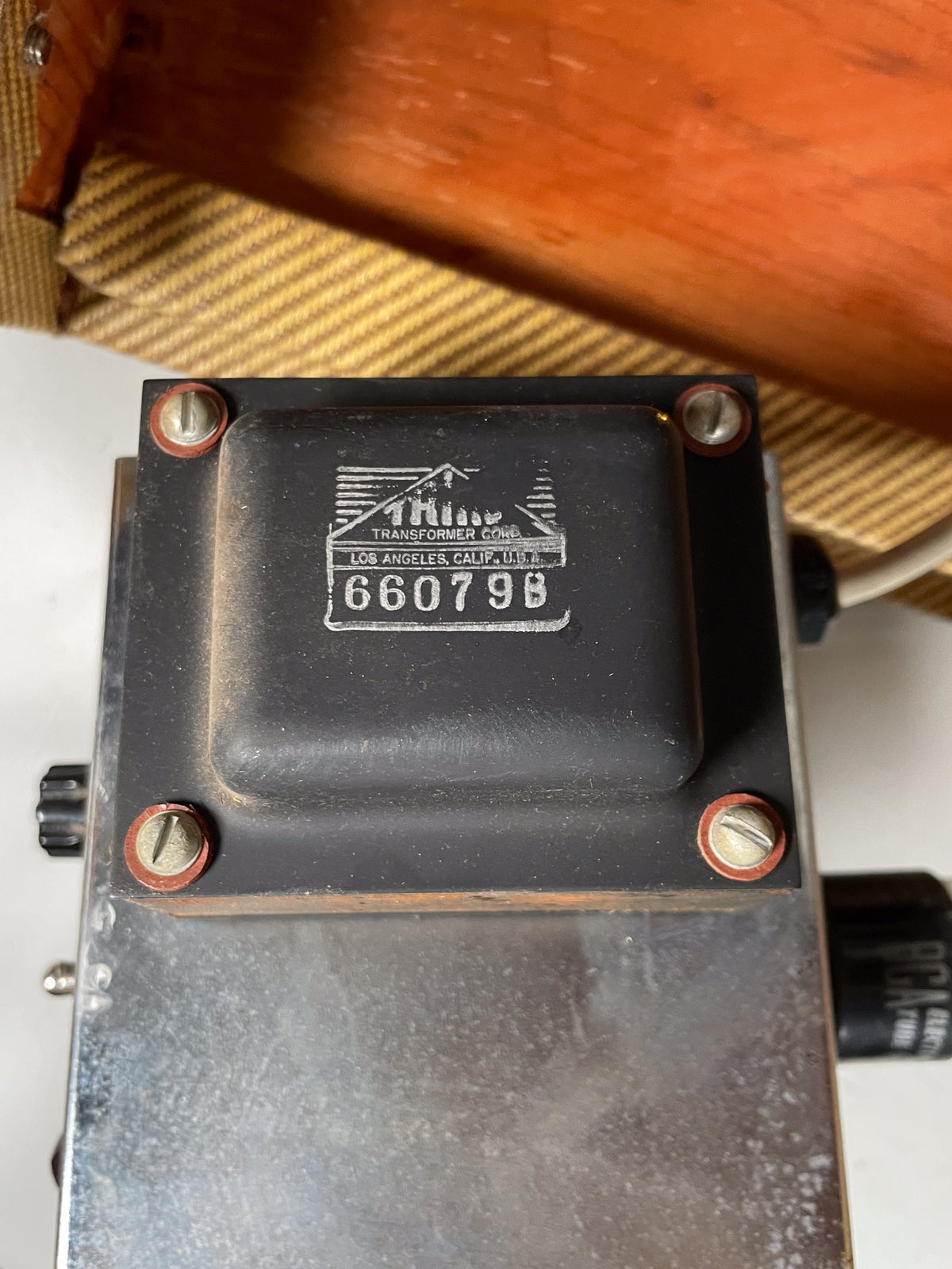 Close-up of the amp's black transformer, showing its silver serial number and four mounting screws with red washers, atop a dusty chrome chassis.