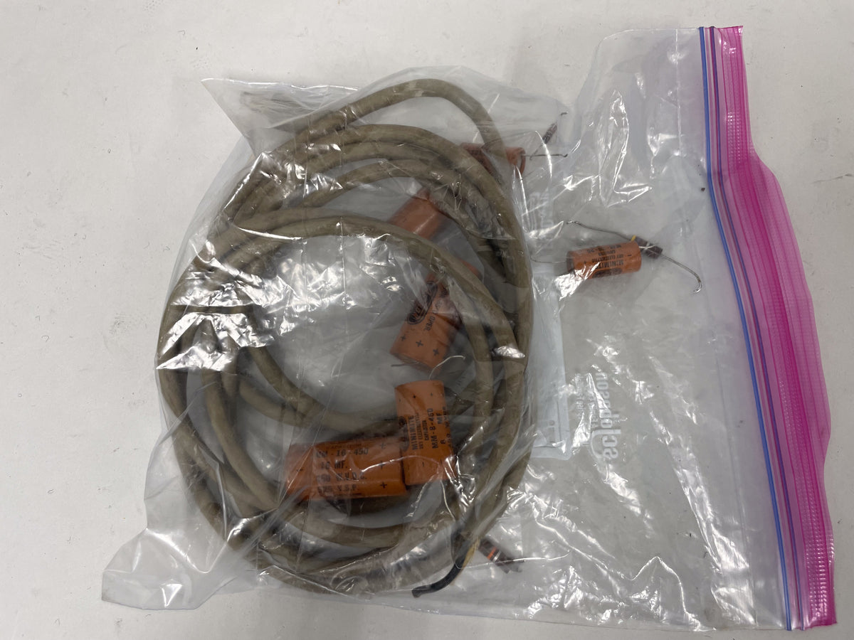 Overhead view of a clear plastic bag containing coiled, tan-braided wire and several orange capacitors with leads.