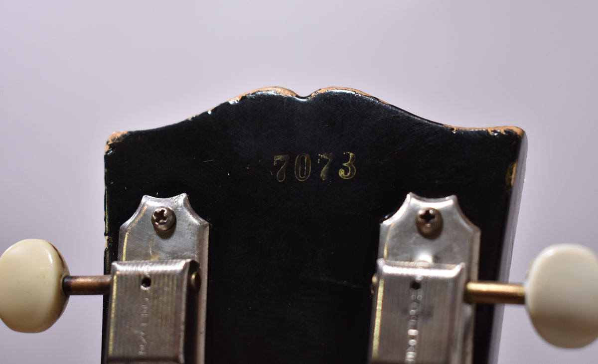 Close-up of the guitar's black headstock with a gold "7073" serial number and two tuners with cream buttons.