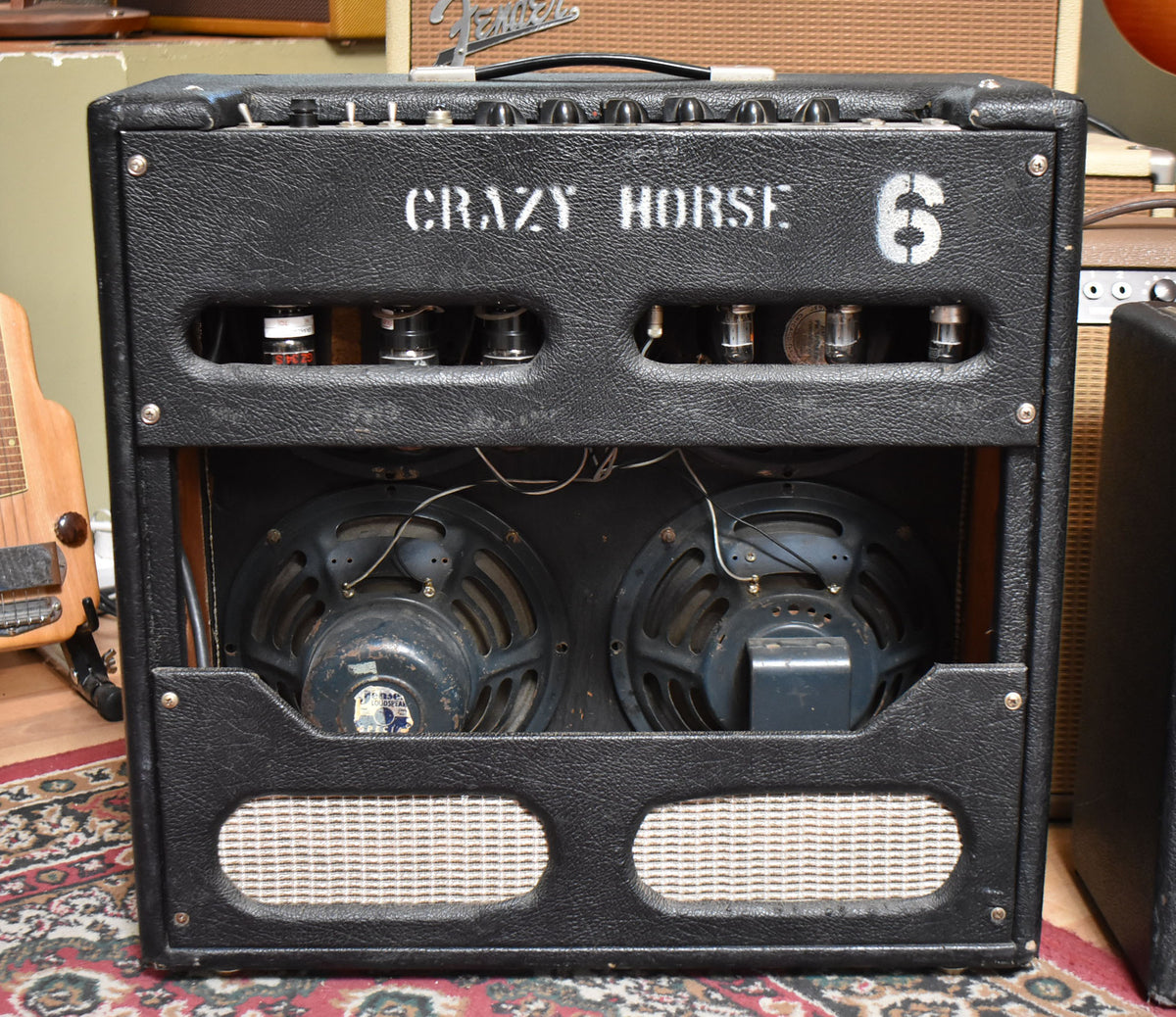 Black "CRAZY HORSE 6" guitar amp with visible tubes and two speakers, on a patterned rug.